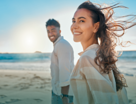 Happy, smiling couple walking down the beach together on a sunny day and enjoying a popular summer date idea.