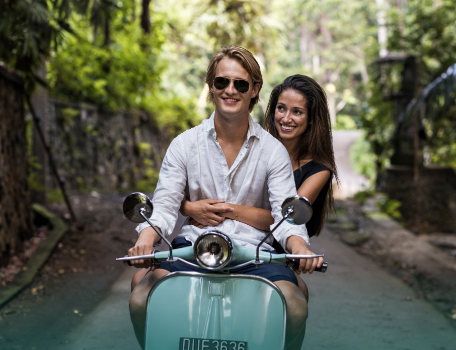 Happy, smiling couple riding a Vespa together on a sunny day while woman is thinking if he is the one.