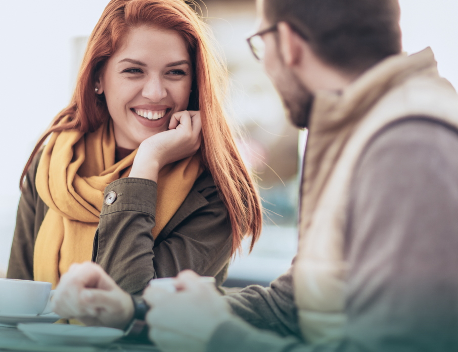 Happy, smiling man and woman enjoying a date in a coffee shop while thinking about first date conversation tips.