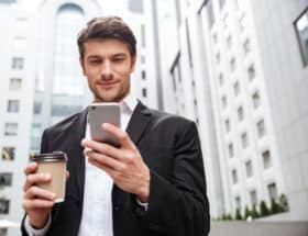 Handsome, well-dressed young man in urban setting, holding his phone and a coffee to go.