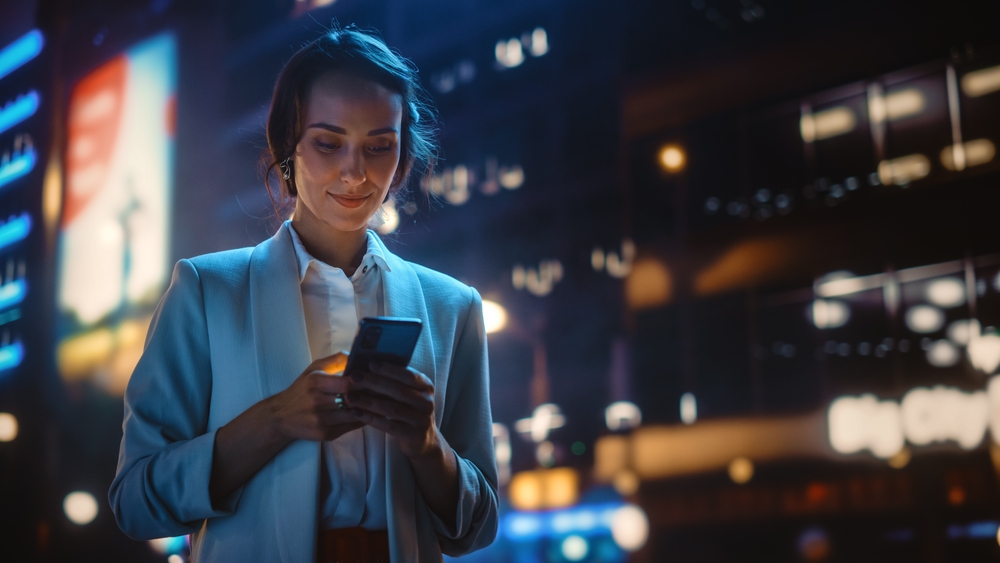 Woman using the phone while walking in the city at night.